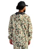 Man wearing a camouflage HUK jacket and hat on a white background