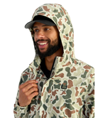 Man wearing a camouflage HUK jacket and hat on a white background