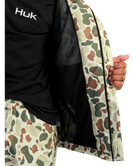 Person wearing a camouflage jacket with Huk logo on a white background