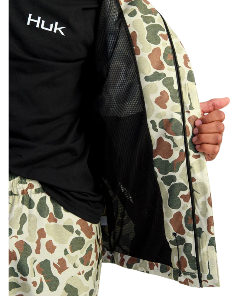 Person wearing a camouflage jacket with Huk logo on a white background