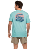 Man wearing a light blue t-shirt with a graphic design on the back, standing against a white background.