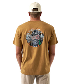 Man wearing a light brown t-shirt with a colorful dog and duck design on the back, standing against a white background.