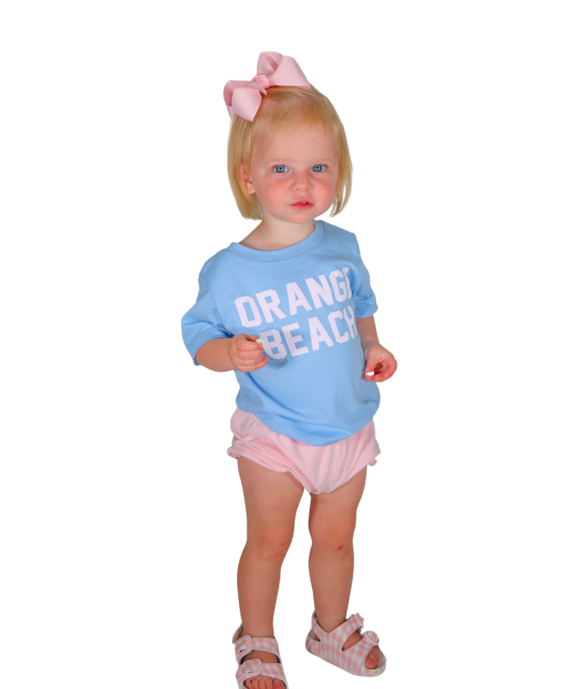 Child wearing a blue 'Orange Beach' shirt and pink shorts on a white background