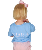 Child wearing a blue shirt with 'SHADES' text, standing against a white background