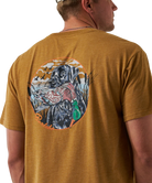 Man wearing a light brown t-shirt with a black dog and duck graphic on the back.