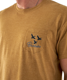 Close-up of a light brown t-shirt with a pocket design featuring birds and text.