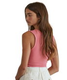 Woman wearing a pink sleeveless top and white pants on a white background