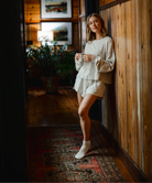 Woman in a cozy indoor setting holding a mug, wearing a light outfit.