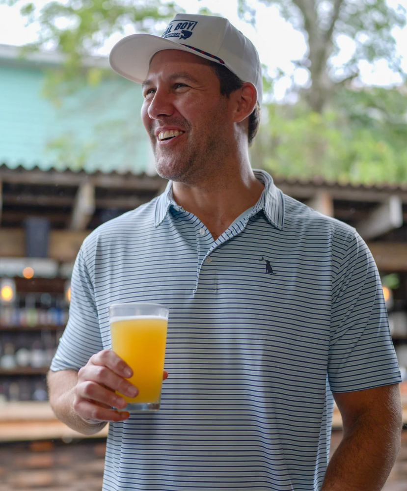 Man wearing a local boy polo holding a glass of beverage outdoors with a blurred background