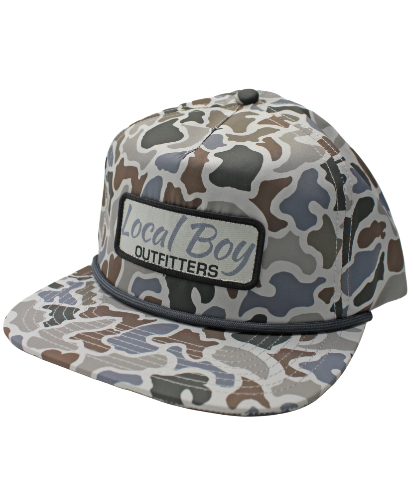 A flat-brim baseball cap with a gray, brown, and beige camouflage pattern, featuring a front patch that reads 'Local Boy OUTFITTERS'.