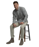 Man sitting on a stool wearing a plaid shirt, beige pants, and brown boots on a white background