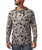 A man wearing a long-sleeve camouflage hoodie in shades of gray, beige, and black, paired with blue jeans, shown from the waist up against a plain white background.