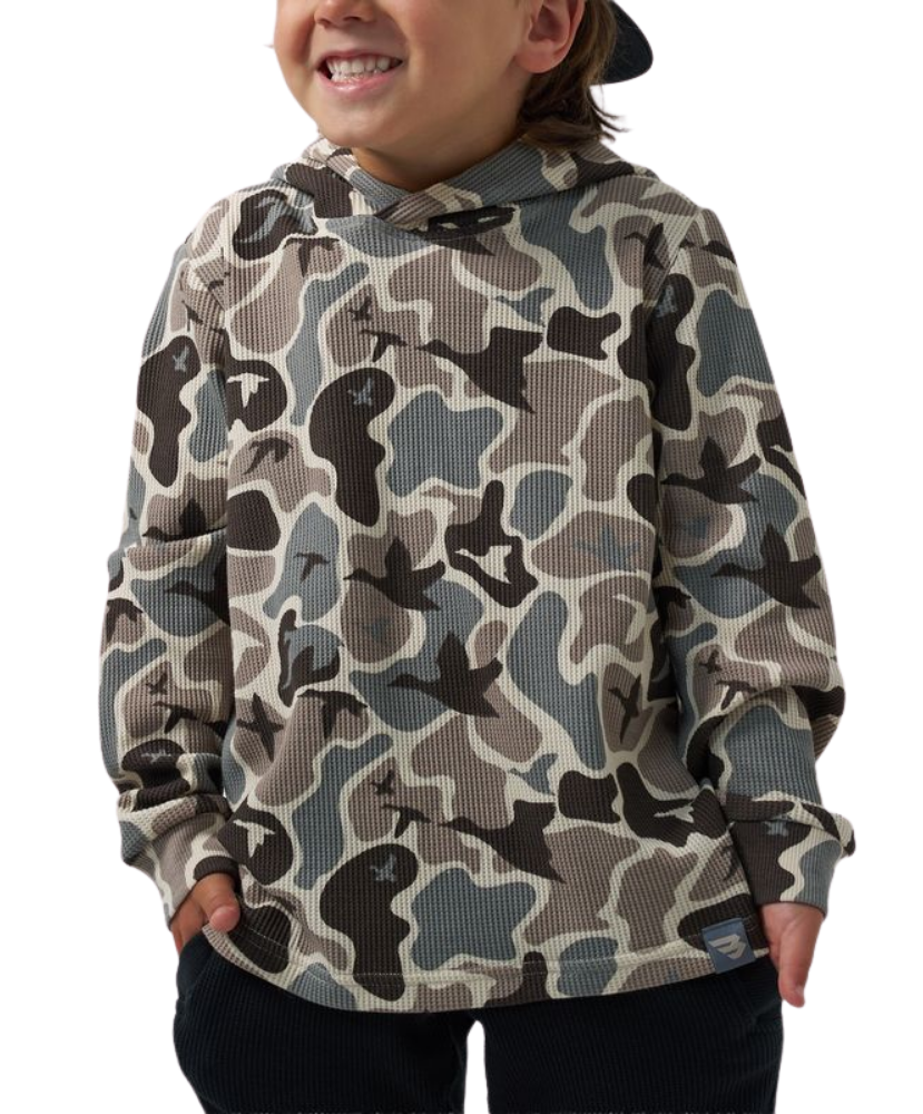 A child wearing a waffle-knit hoodie with a muted camouflage pattern in beige, gray, and black, paired with dark pants against a plain white background.