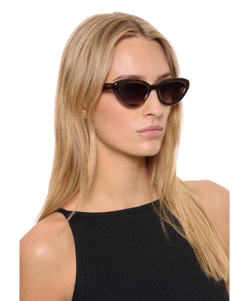 Woman wearing cat-eye Krewe sunglasses with a plain background
