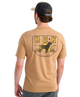 Man wearing a tan HUK shirt with a logo on the back, standing against a white background