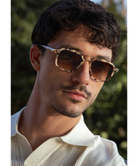 Man wearing tortoise Krewe print sunglasses with a blurred green background