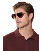 Man wearing brown Krewe sunglasses and a maroon polo shirt on a white background