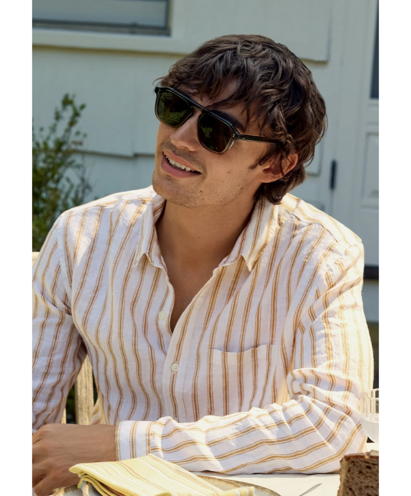 Man wearing Krewe sunglasses and a striped shirt sitting outdoors.