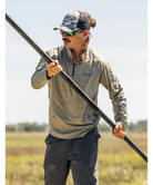 Man holding a long pole in an outdoor setting wearing a Huk shirt.