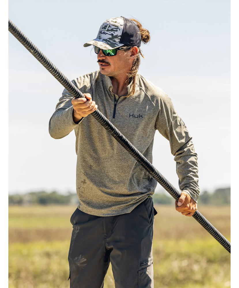 Man holding a long pole in an outdoor setting wearing a Huk shirt.