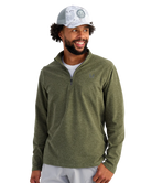 Man wearing a green HUK pullover and white cap on a white background