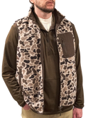 Man wearing a brown jacket with a camouflage vest over it on a white background