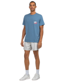 Man wearing a blue t-shirt with a logo and white shorts on a white background
