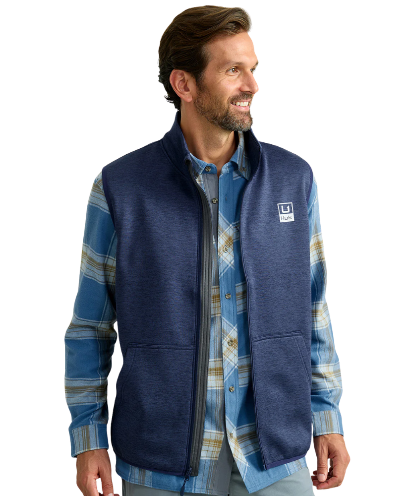 Man wearing a blue fleece vest over a plaid shirt on a white background HUK GEAR VEST