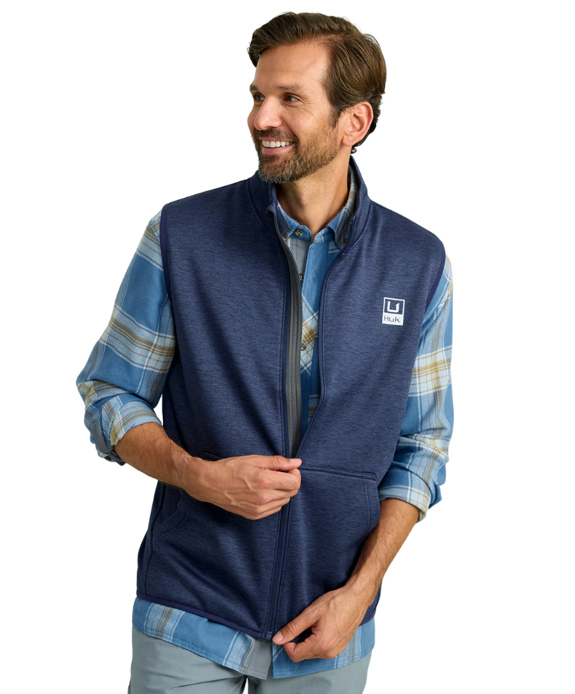 Man wearing a blue fleece vest over a plaid shirt on a white background HUK GEAR VEST