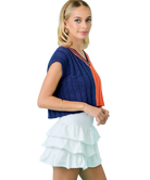 Woman wearing a blue and orange top with a white ruffled skirt on a white background