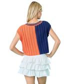 Woman wearing a two-tone orange and blue sweater with a white skirt on a white background