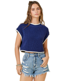 Woman wearing a blue knit top and denim shorts on a white background