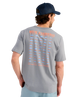 Man wearing a gray t-shirt with fishing-themed design on the back, standing against a white background.