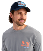 Man wearing a navy cap and gray shirt with 'Huk Fishing' logo on a white background
