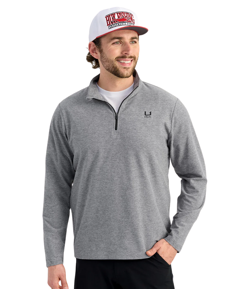 Man wearing a gray pullover with a HUK logo and a cap on a white background