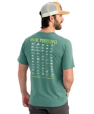 Man wearing a green Huk Fishing t-shirt with fish illustrations on the back.
