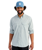 Man wearing a light blue HUK button-up shirt and blue cap on a white background
