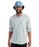 Man wearing a light blue HUK button-up shirt and blue cap on a white background