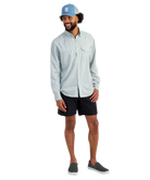 Man wearing a light blue HUK button-up shirt and blue cap on a white background