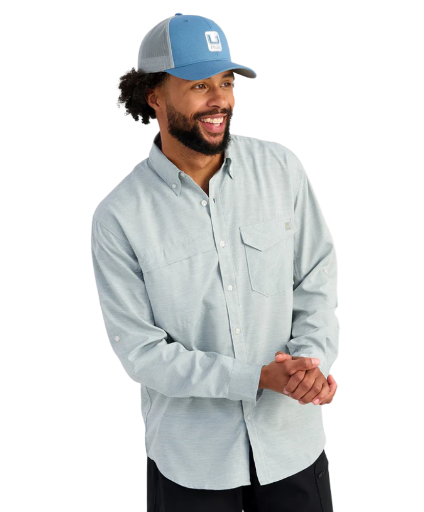 Man wearing a light blue HUK button-up shirt and blue cap on a white background