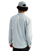 Man wearing a light blue HUK button-up shirt and blue cap on a white background