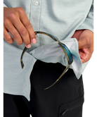 Person cleaning a pair of glasses with a light blue button up Huk shirt and black pants.