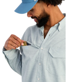 Man wearing a light blue shirt with a pocket, holding a small object.