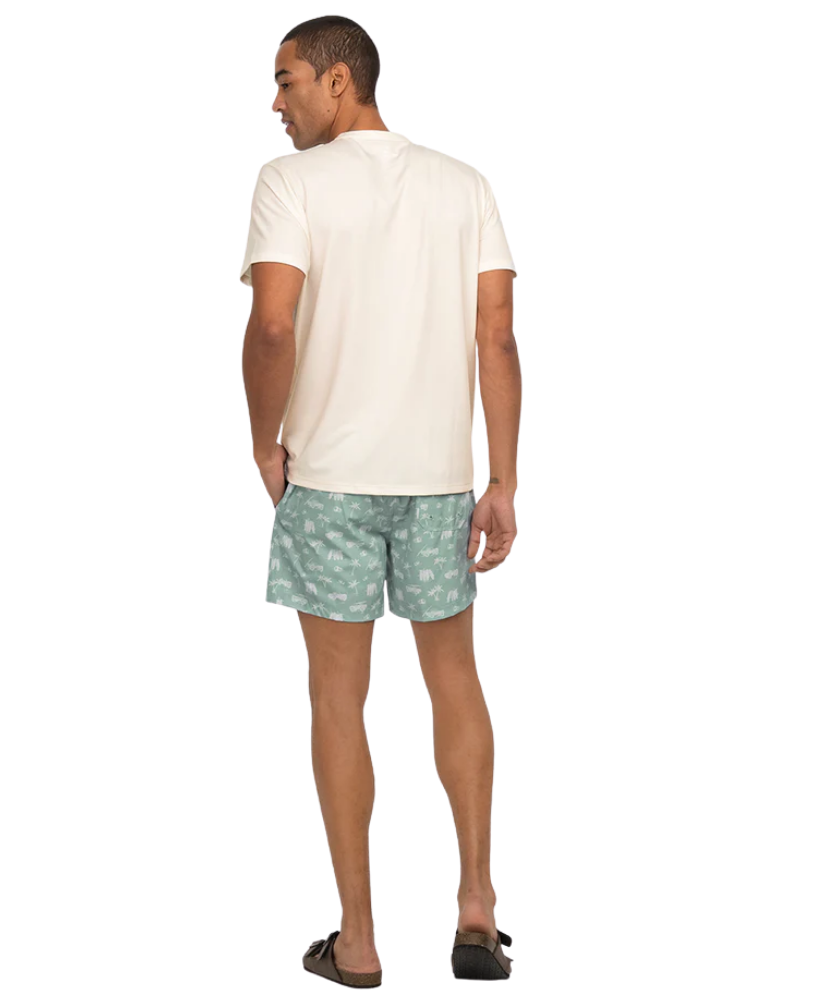 Man wearing a white henley t-shirt and green patterned shorts on a white background