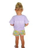 Child wearing a purple shirt with 'SHADES' text and floral shorts on a white background