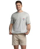 Man wearing a gray t-shirt with a logo and beige shorts on a white background