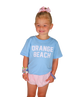 Young girl wearing a light blue 'Orange Beach' t-shirt and pink shorts on a white background