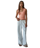 Woman wearing a pink tank top and light blue pants on a white background