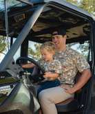 Man and child sitting inside a vehicle with trees in the background