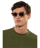 Man wearing Krewe sunglasses and a green sweater on a white background